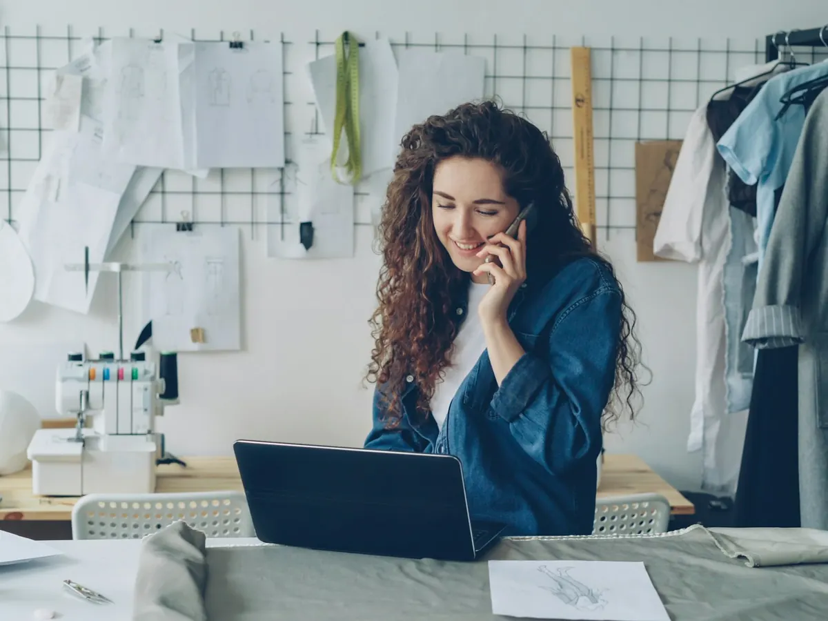 Selbstständige Designerin telefoniert in ihrem Atelier am Laptop